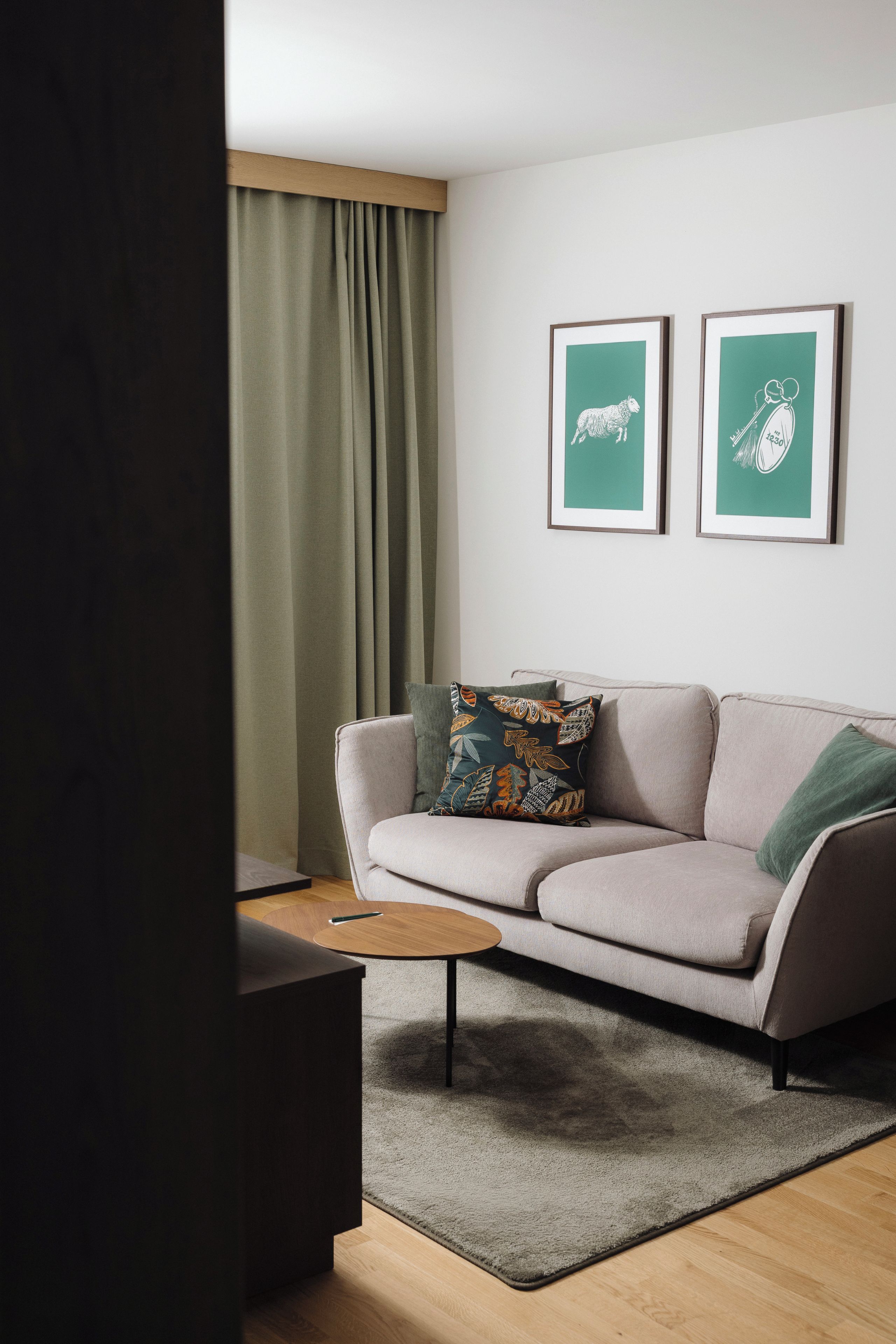 A modern living room with a sofa, a coffee table, and a rug. There are two framed pictures on the wall.