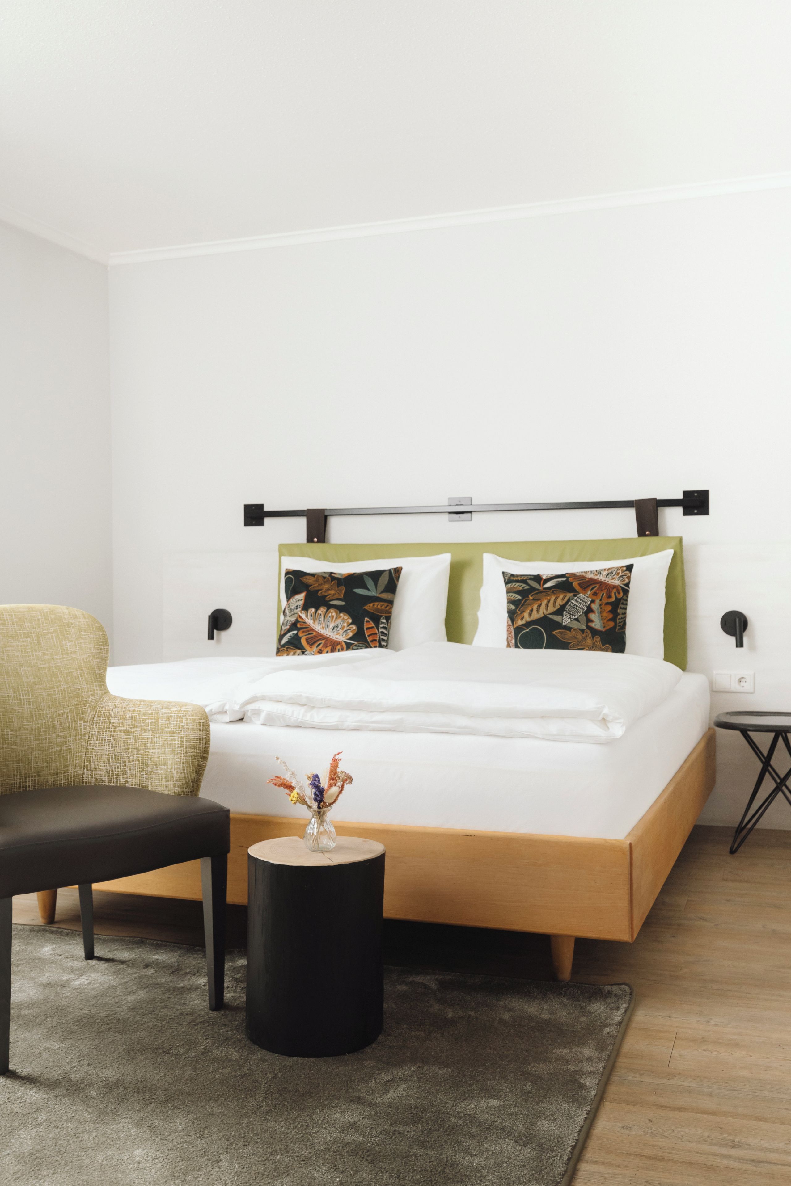 A modern bedroom with a bed, a bench, a small table, and a wall-mounted nightstand.