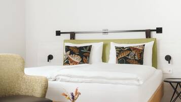 A modern bedroom with a bed, a bench, a small table, and a wall-mounted nightstand.