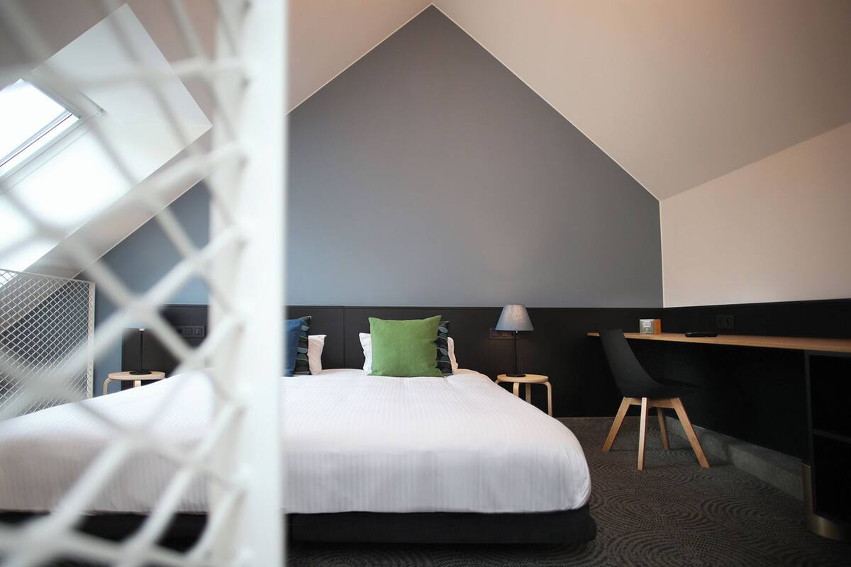 A modern hotel room with a bed, a desk, and a chair.