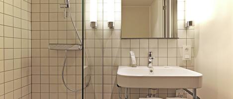 Un baño moderno con ducha envuelta en vidrio, un lavamanos blanco y dos toallas colgadas en un perchero metálico.