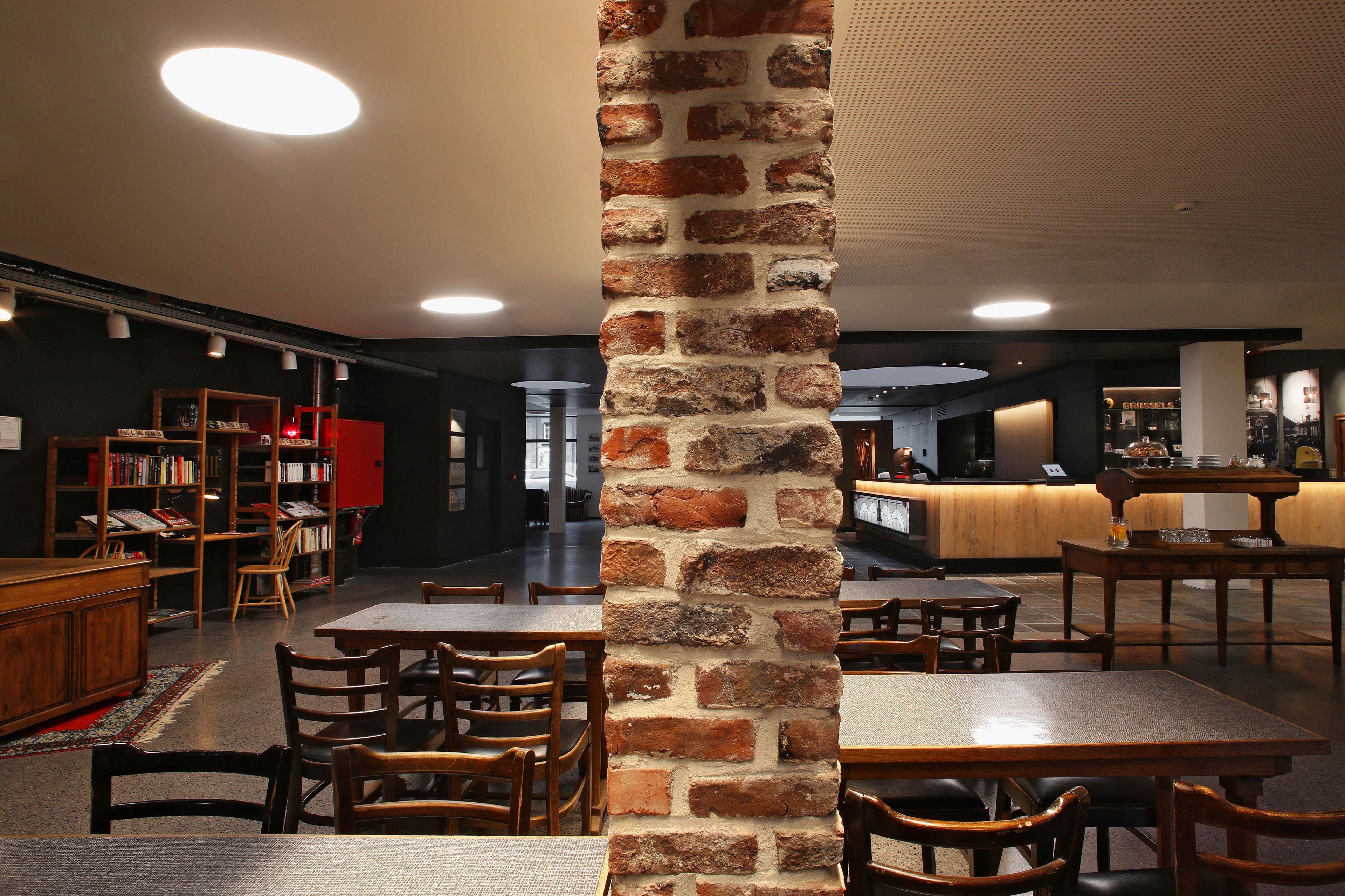 A restaurant with brick pillars, wooden tables, and chairs. There is a counter with a menu and a bar area in the background.
