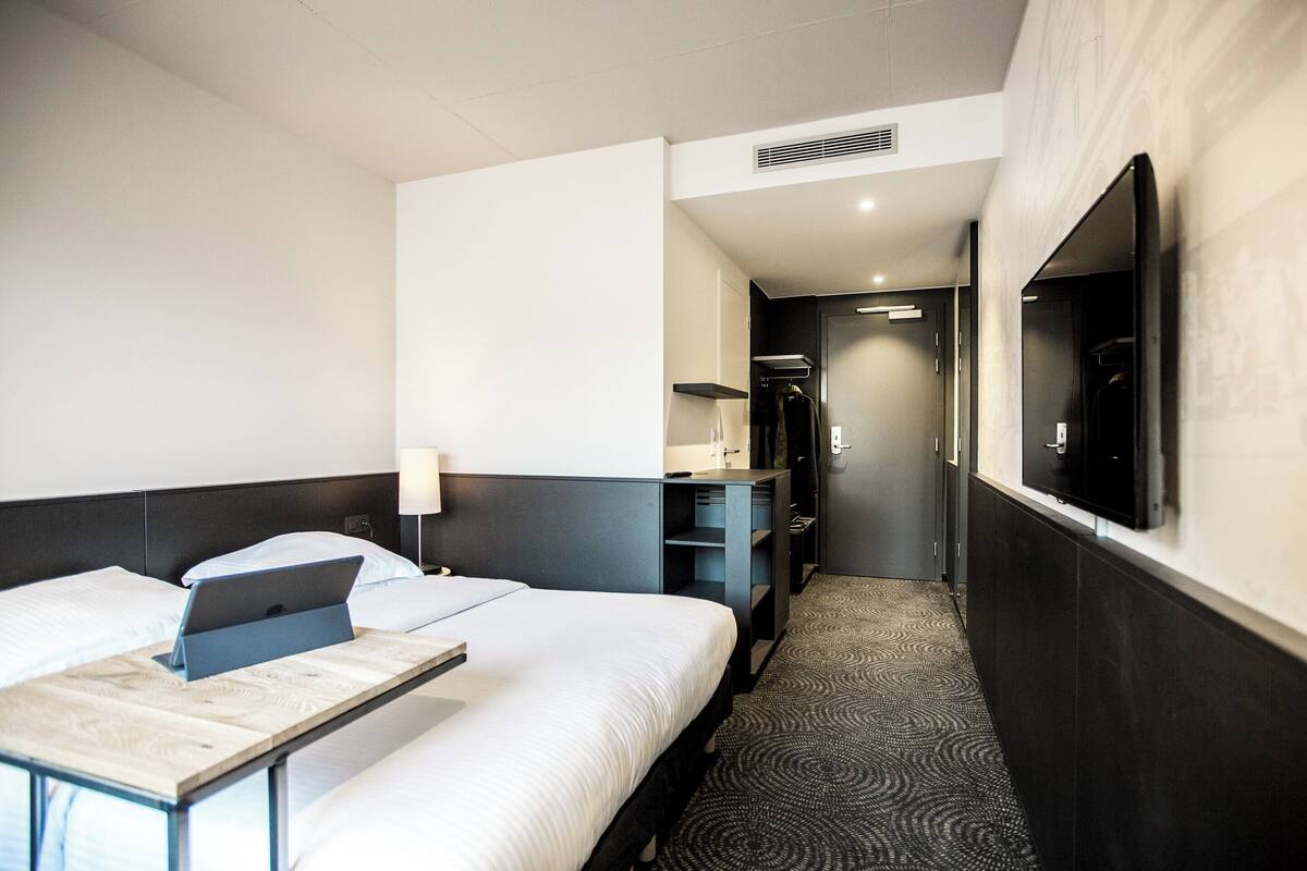 A hotel room with two beds, a desk with a laptop, a TV, and a walk-in closet.