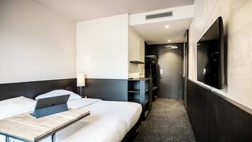 Een hotelkamer met twee bedden, een bureau met een laptop, een televisie en een inloopkast.