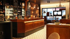 A bar area with a wooden counter, shelves with bottles, glasses, and a menu board. - Hôtel Van Belle (Brussels)