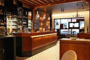 A bar area with a wooden counter, shelves with bottles, glasses, and a menu board.