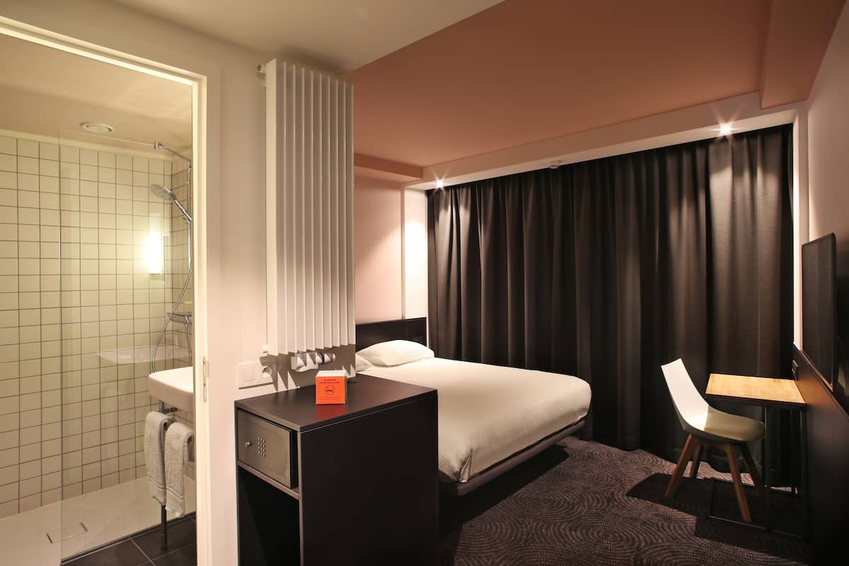 A hotel room with a shower, a bed, a desk, and a chair.