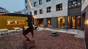 An outdoor courtyard with tables and chairs, string lights, and a sculpture. - Hôtel Van Belle (Brussels)