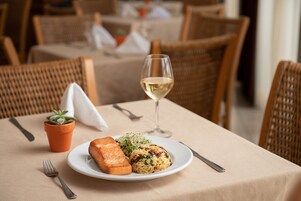 Una mesa de comedor con un plato de comida, una copa de vino blanco y una pequeña planta en maceta.