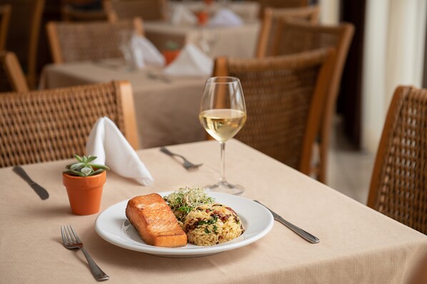 A dining table with a plate of food, a glass of white wine, and a small potted plant. - Intercity Florianópolis (Florianópolis)