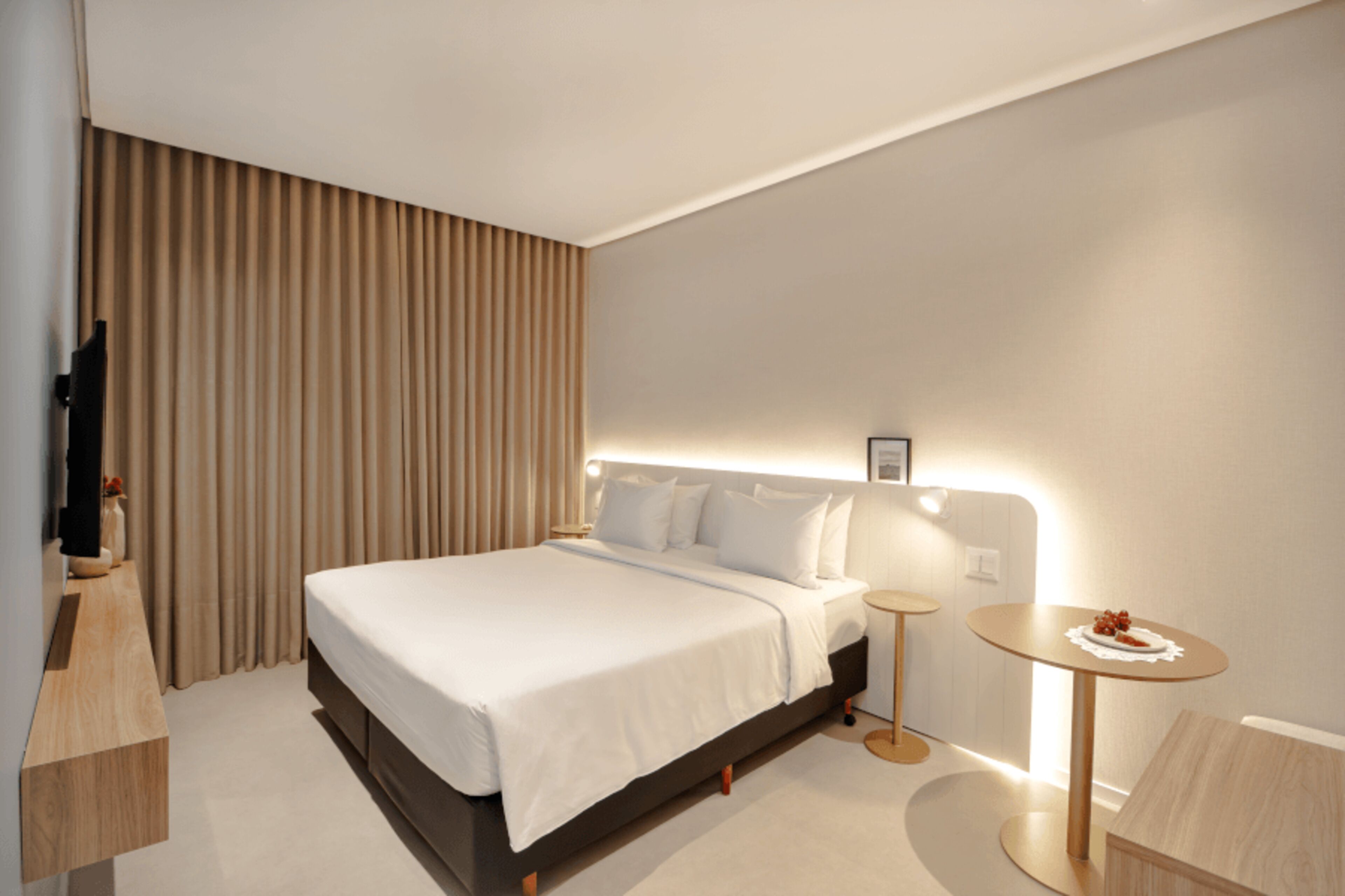 Quarto de hotel moderno com uma cama grande, mesas de cabeceira, uma pequena mesa redonda e uma televisão.