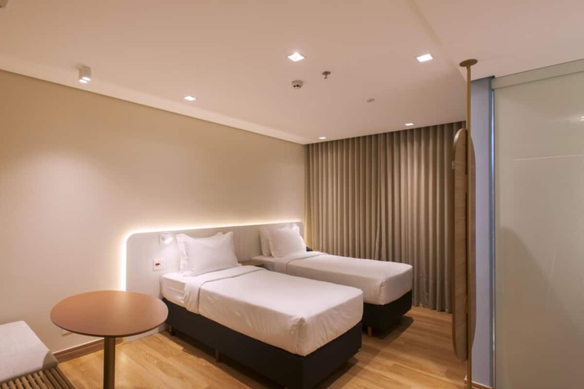 Une chambre d’hôtel avec deux lits, une table ronde et une porte coulissante.