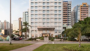 A multi-story hotel with a modern facade, a prominent entrance, and a parking area in front.