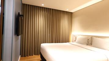 Una camera d'hotel con un letto grande, una televisione fissata al muro e una finestra coperta da tende.