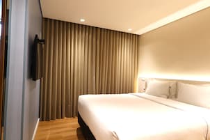 Una camera d'hotel con un letto grande, una televisione fissata al muro e una finestra coperta da tende.