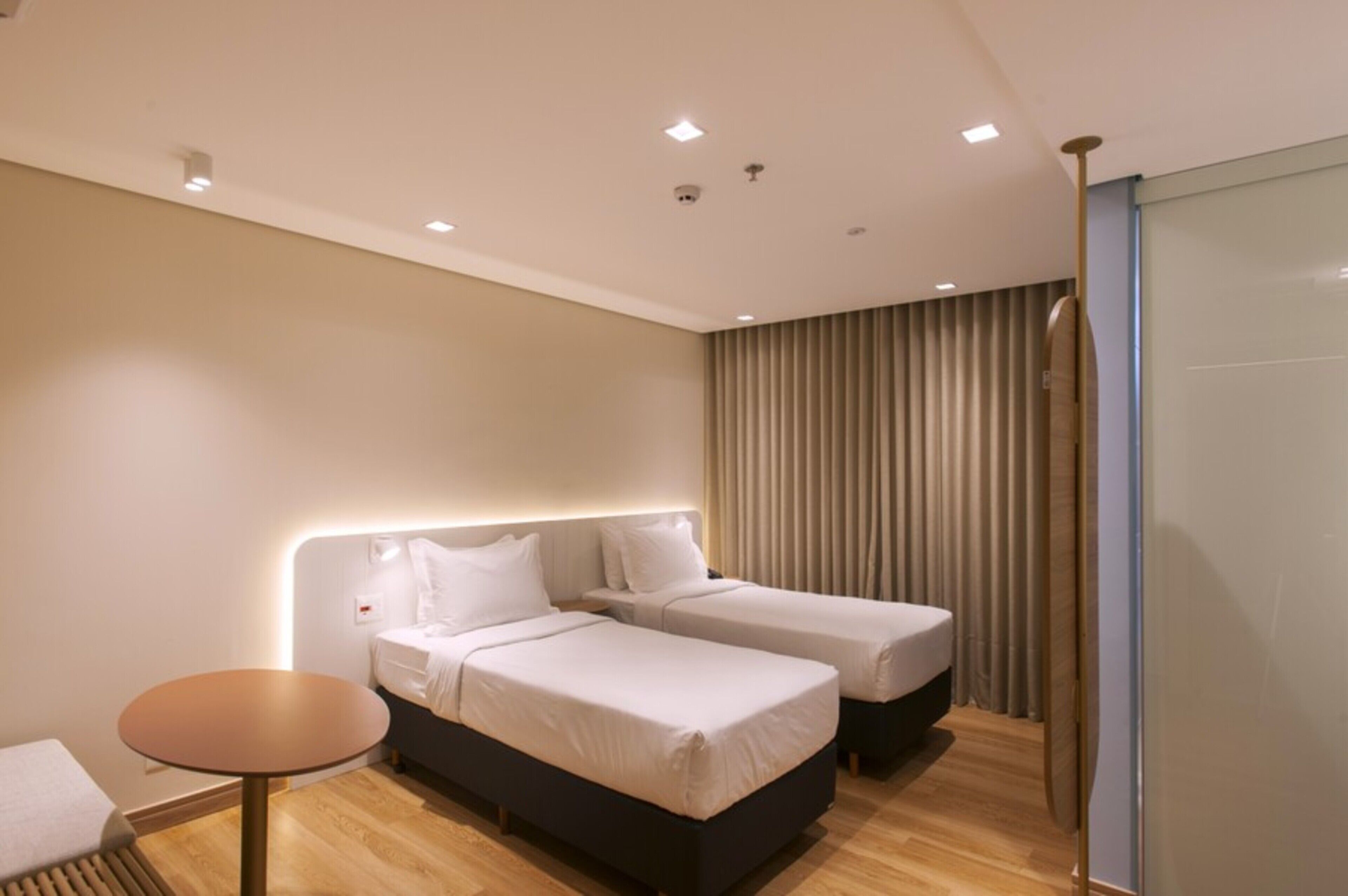 A hotel room with two beds, a round table, and a curtain-covered window.