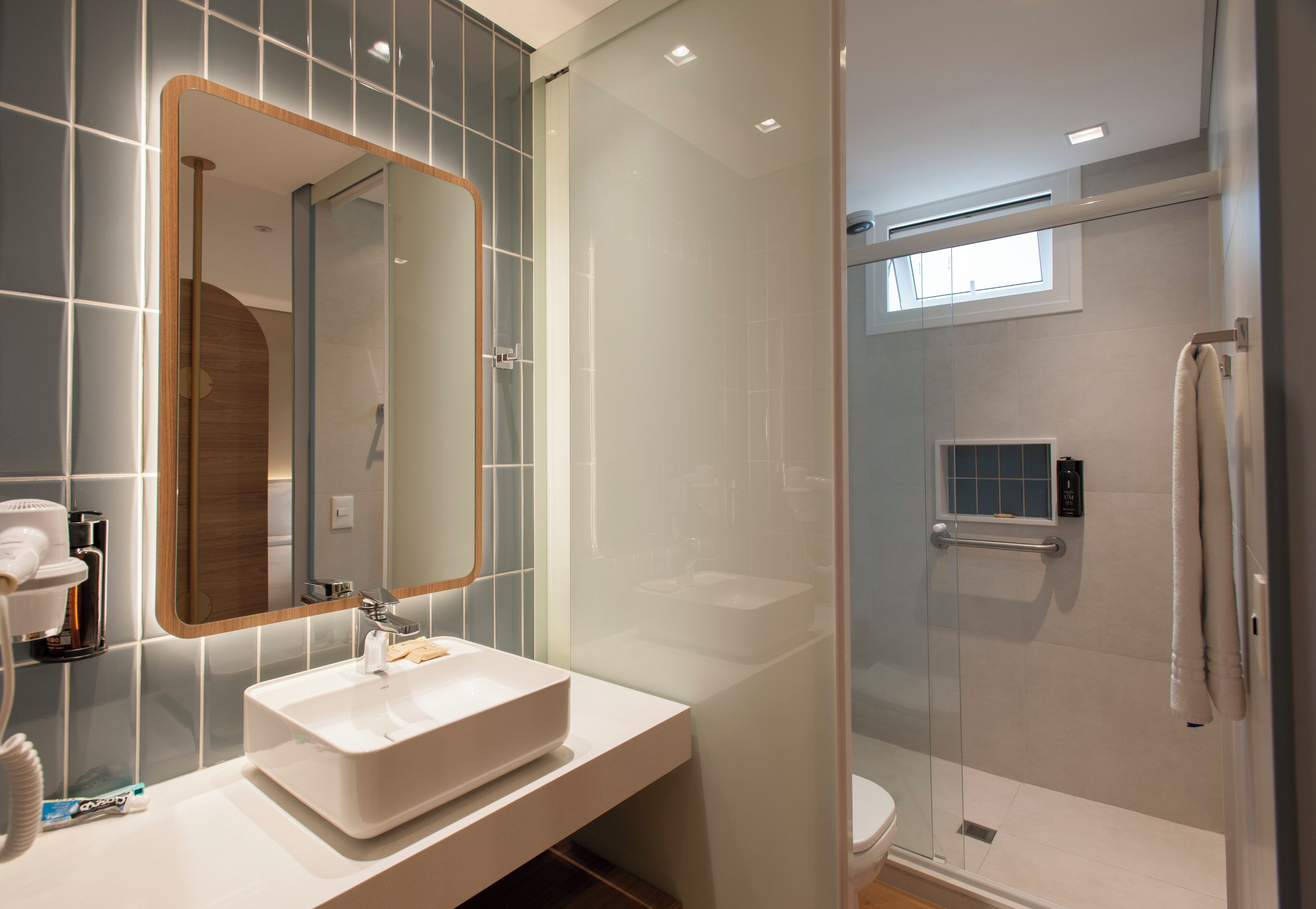 A modern bathroom with a large mirror, a white sink, and a glass-enclosed shower.