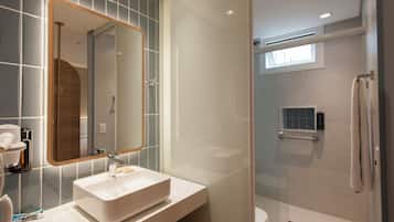 A modern bathroom with a large mirror, a white sink, and a glass-enclosed shower.