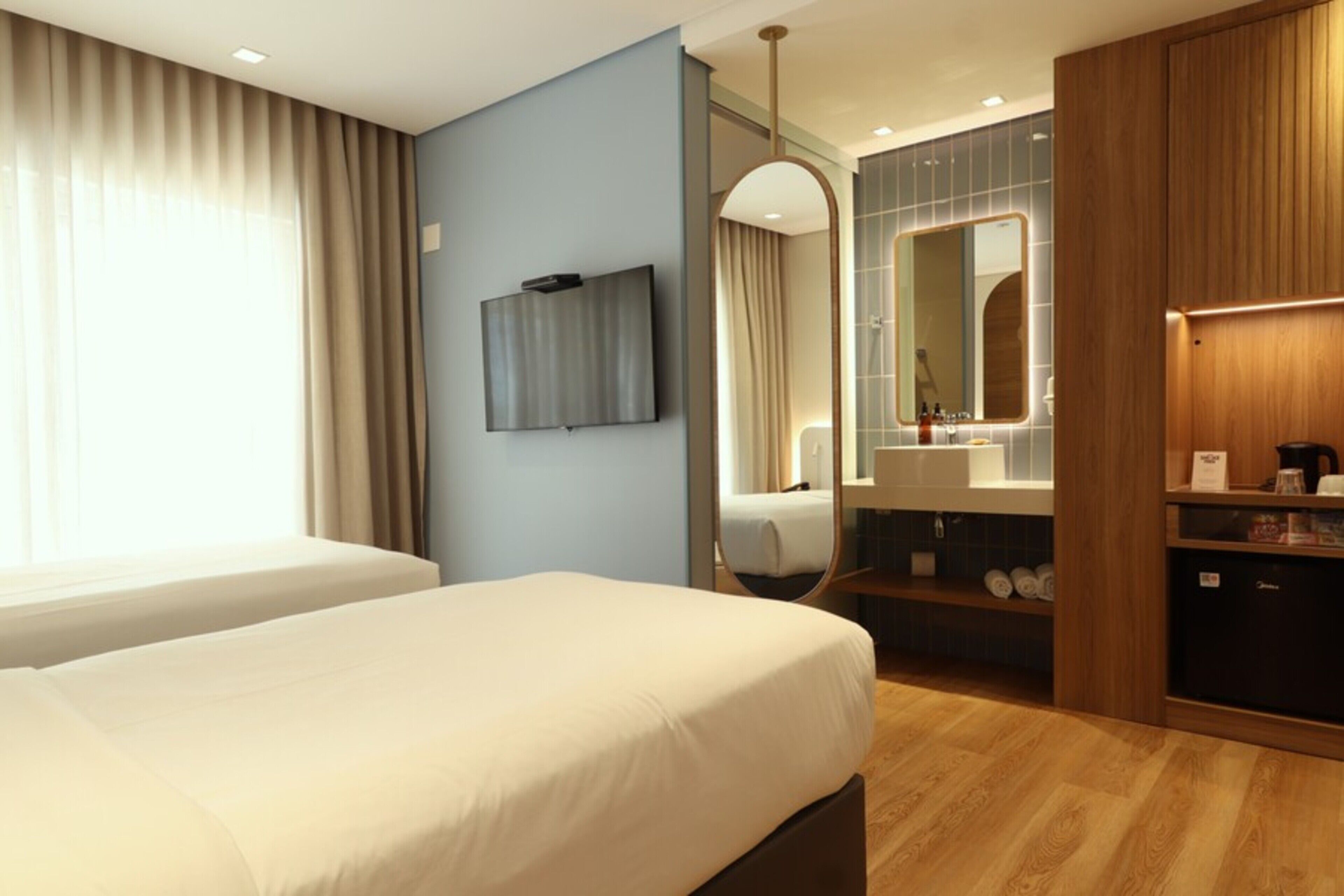 Ein Hotelzimmer mit Bett, Fernseher, Spiegel, Schminktisch mit Waschbecken und Kleiderschrank.