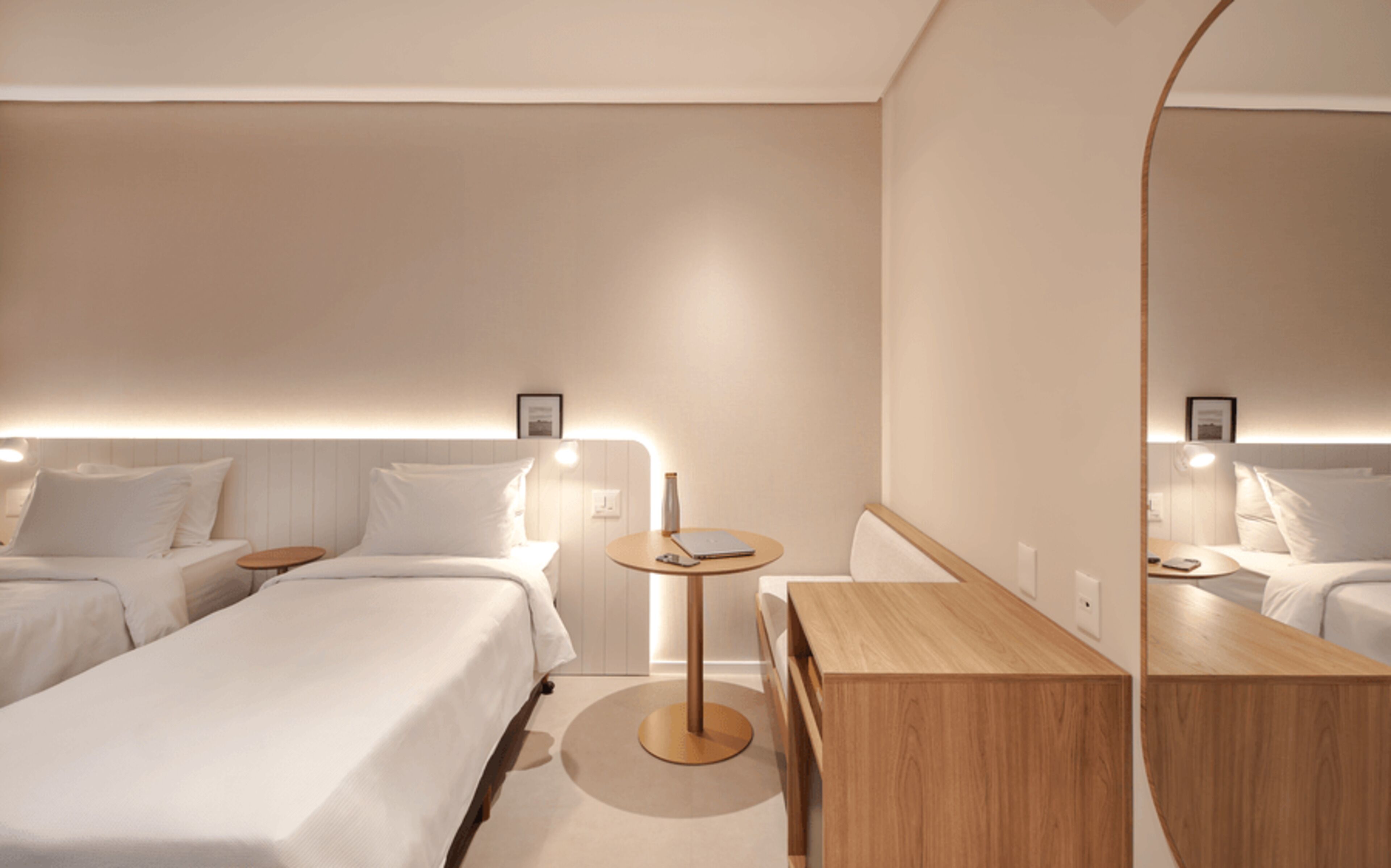 A hotel room with two beds, a wooden desk, a round table, and a large mirror.