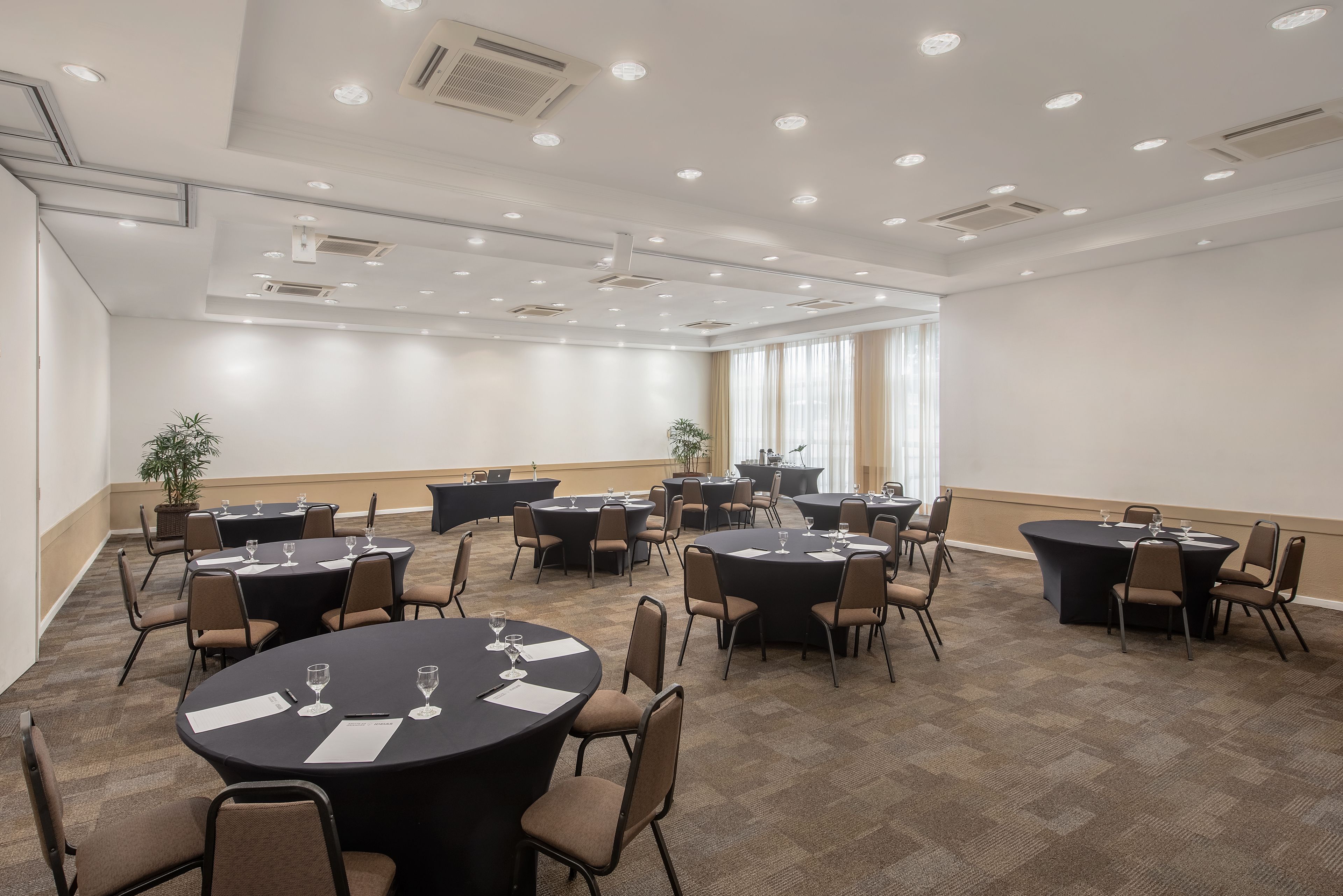 Uma sala de conferências com várias mesas redondas, cada uma com cadeiras e copos de vinho.