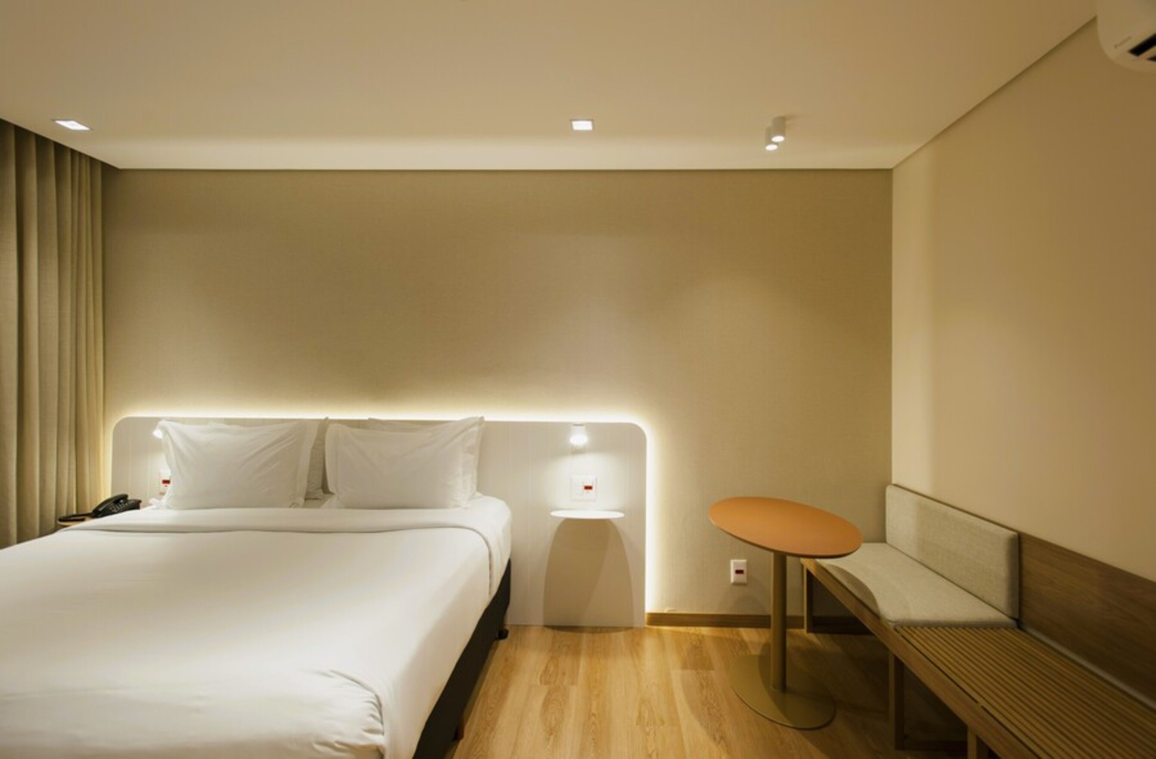 Una habitación de hotel con cama, mesita de noche y un banco.