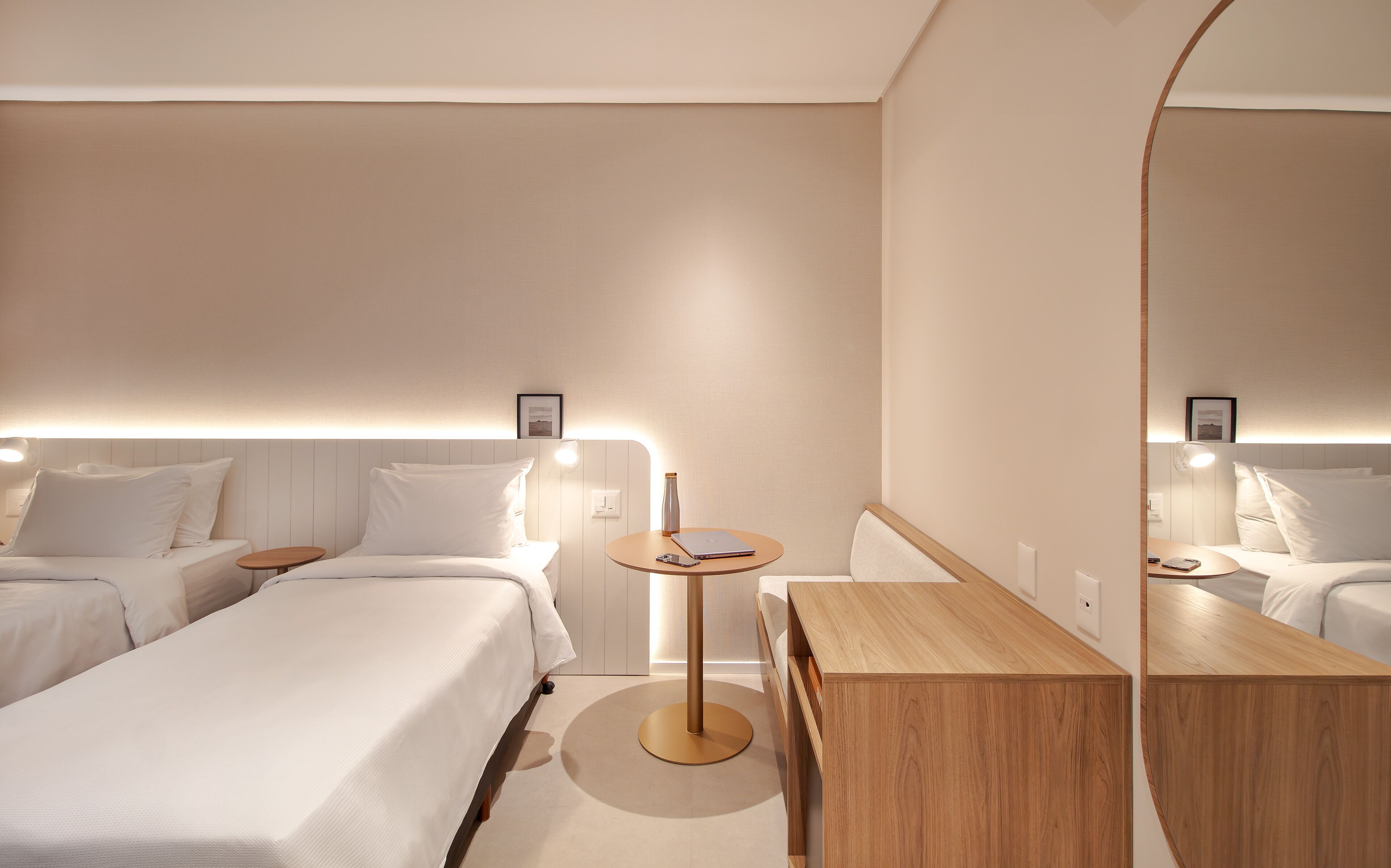 A modern hotel room with a bed, bedside tables, a desk, and a large mirror.