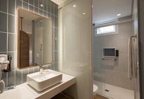 A modern bathroom with a glass shower enclosure, a large mirror, and a white sink.