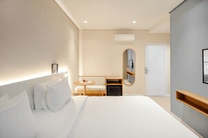 Una camera d'albergo moderna con un letto grande, un tavolino rotondo, uno specchio, un armadio e una porta.