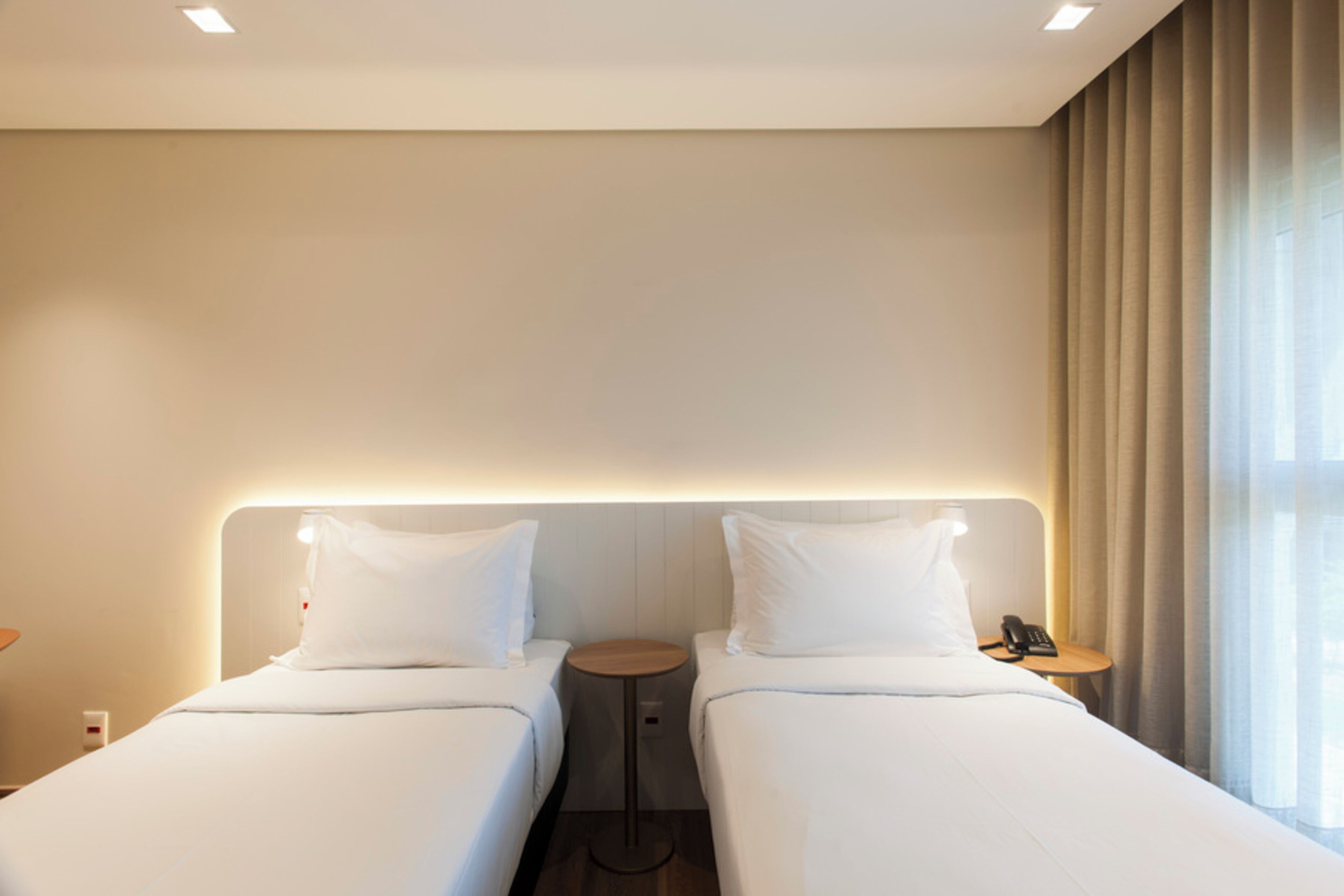 Una camera d'albergo con due letti, un comodino con il telefono e una finestra con tende.