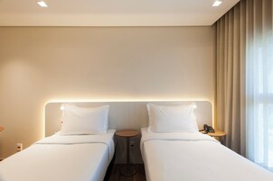 Una camera d'albergo con due letti, un comodino con il telefono e una finestra con tende.