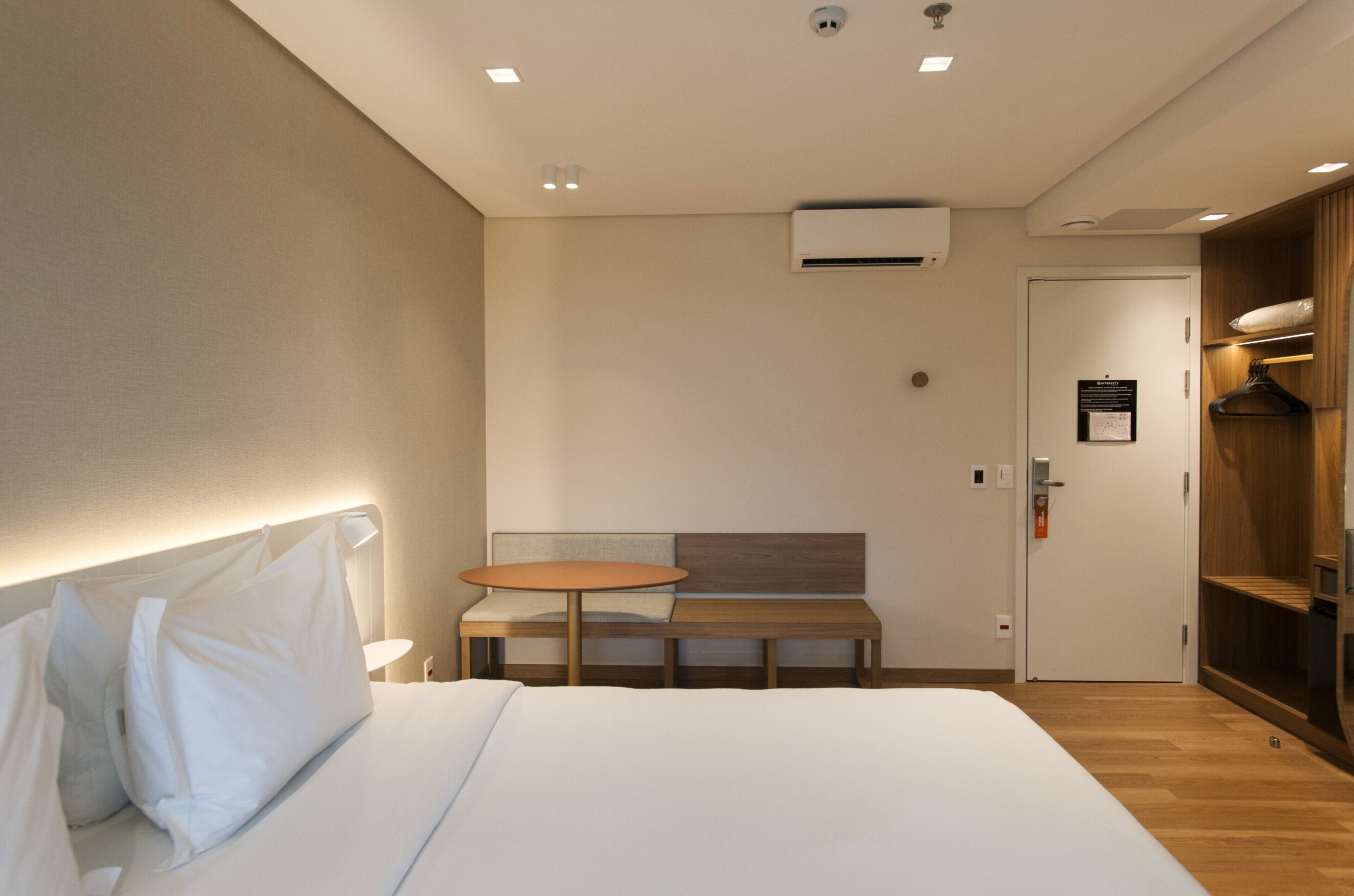 Una camera d'albergo con un letto, un tavolino rotondo, una panca e un armadio in legno.