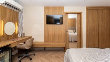 Habitación de hotel moderna con escritorio de madera, una silla cómoda, cama con ropa de cama estampada, televisor de pantalla plana montado en la pared y un armario.