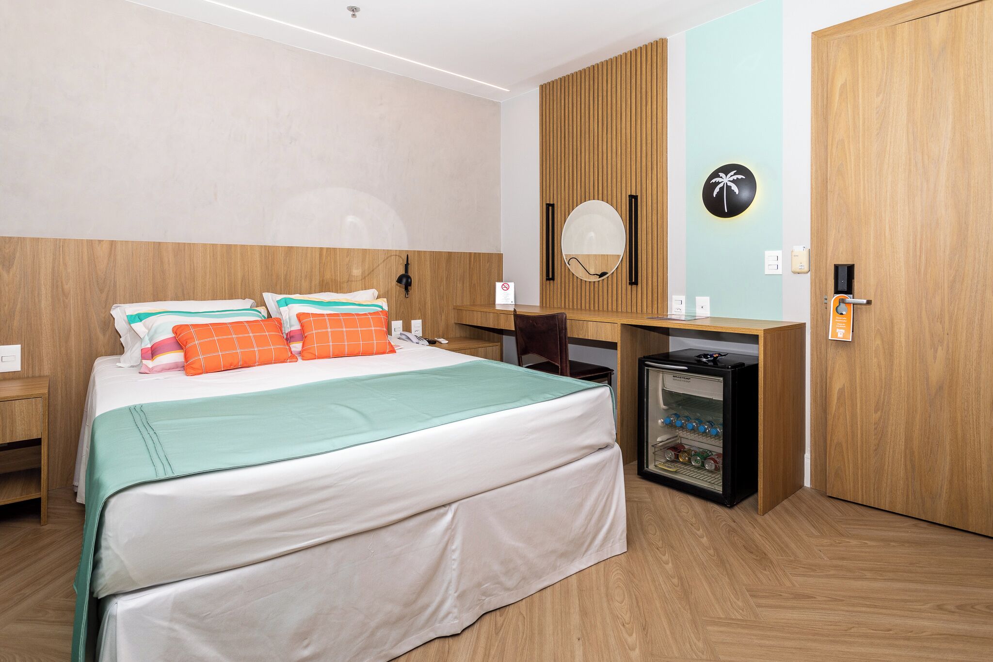 A hotel room with a bed, a desk, a small fridge, and a wooden wardrobe.