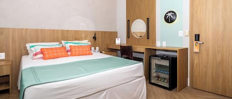 A hotel room with a bed, a desk, a small fridge, and a wooden wardrobe.