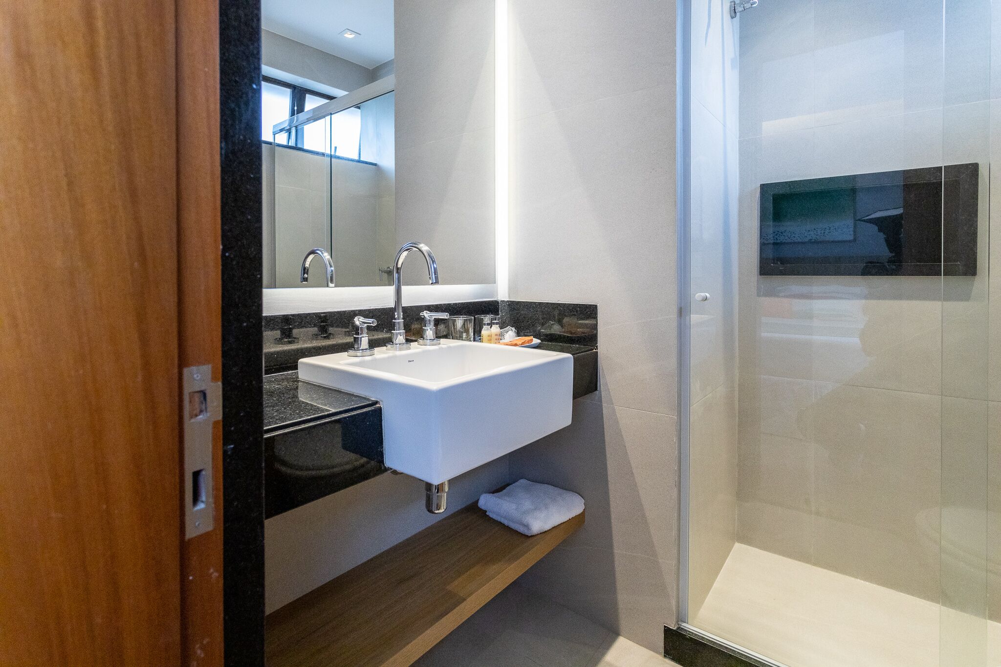 A modern bathroom with a white sink, black countertop, and a glass shower enclosure.