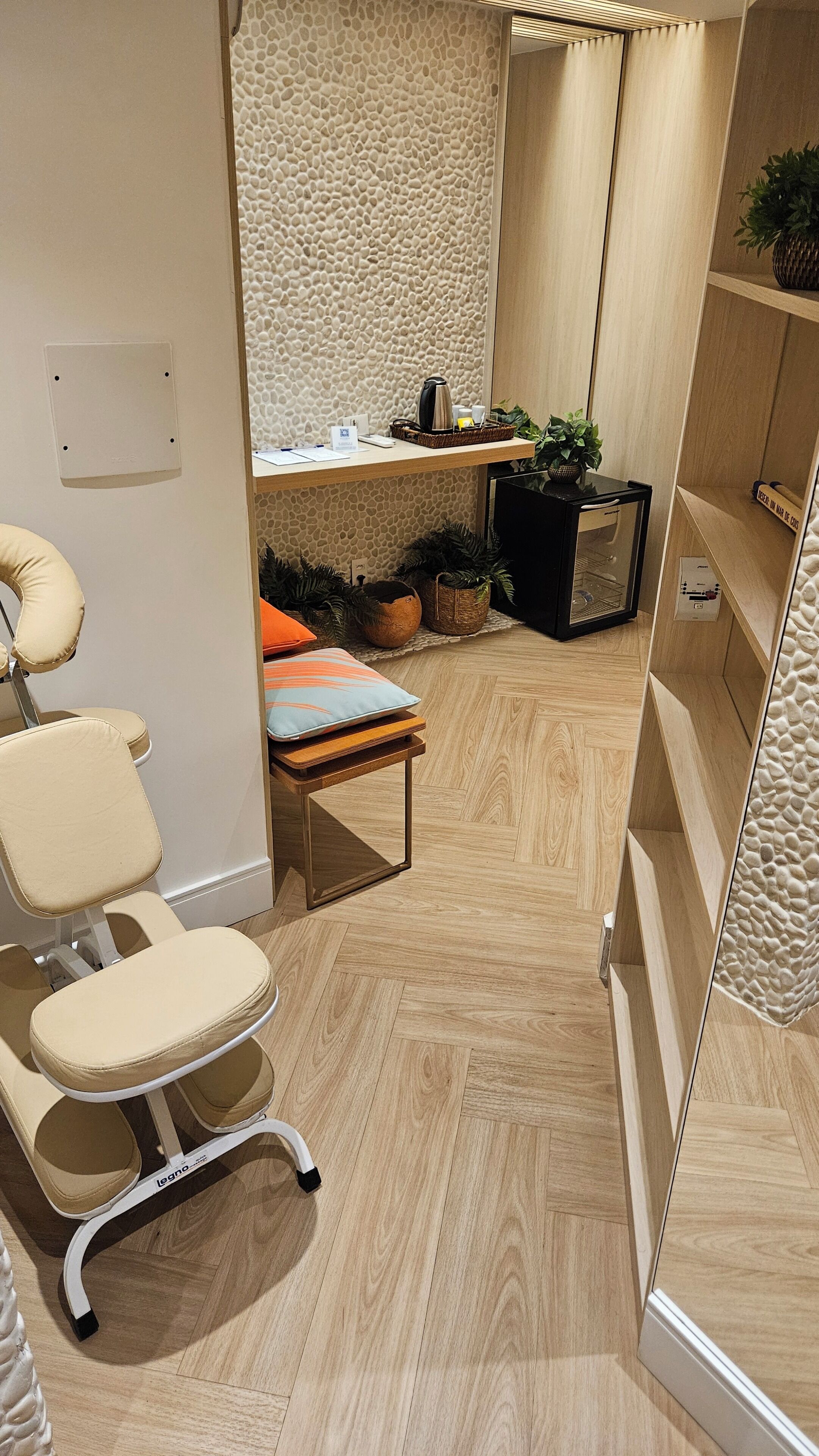 Una habitación moderna con suelo de madera, un sillón acolchado, un escritorio con un cesto y una estantería con una planta.