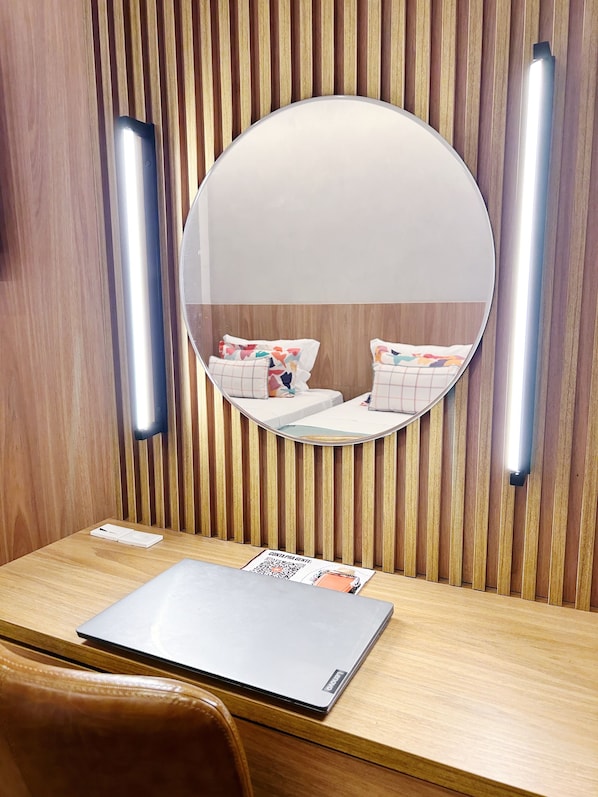 A wooden vanity with a round mirror, a laptop, and a small table with a magazine. - Hotel Astoria Ipanema (Rio de Janeiro)