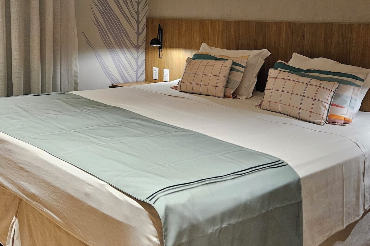 Un dormitorio moderno con una cama grande, una lámpara de noche y una planta en la pared.