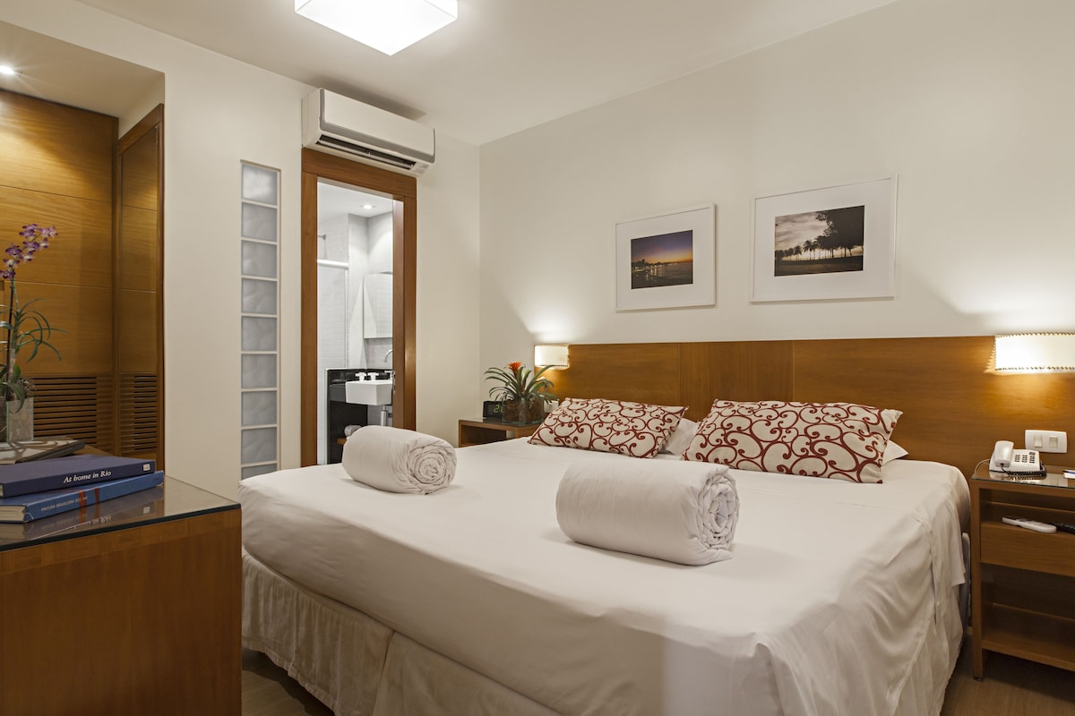 Una cama bien hecha con almohadas, una mesita de noche con lámpara y un teléfono en la pared.