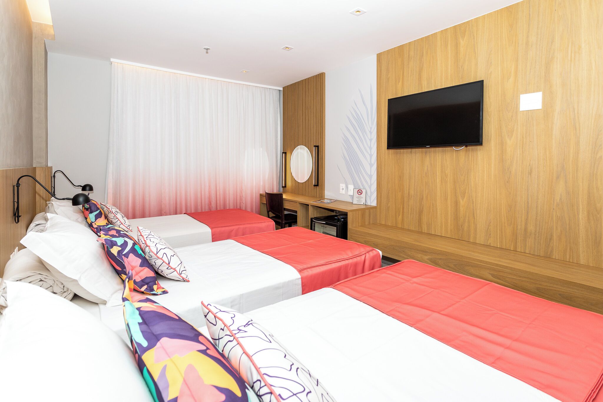 Una habitación de hotel con dos camas, un escritorio, un televisor y un espejo.