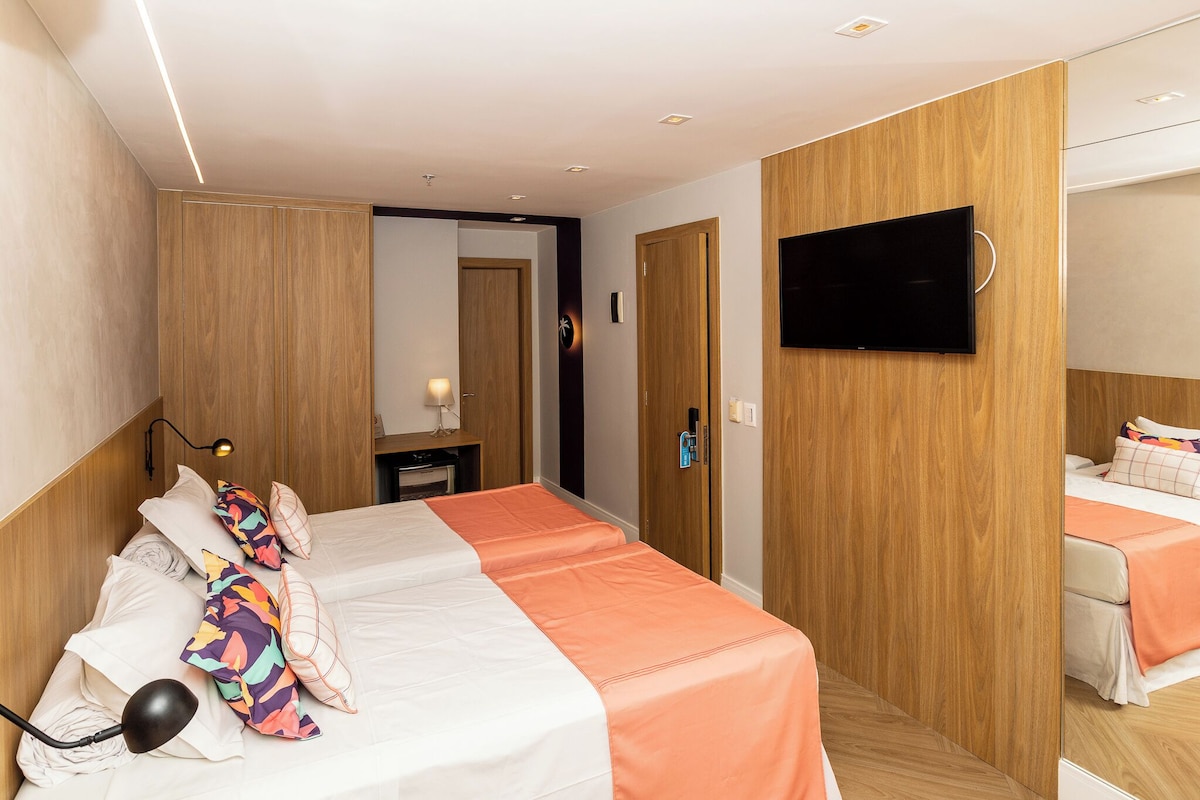 Ein Hotelzimmer mit zwei Betten, einem an der Wand befestigten Fernseher und einem Holzschrank.