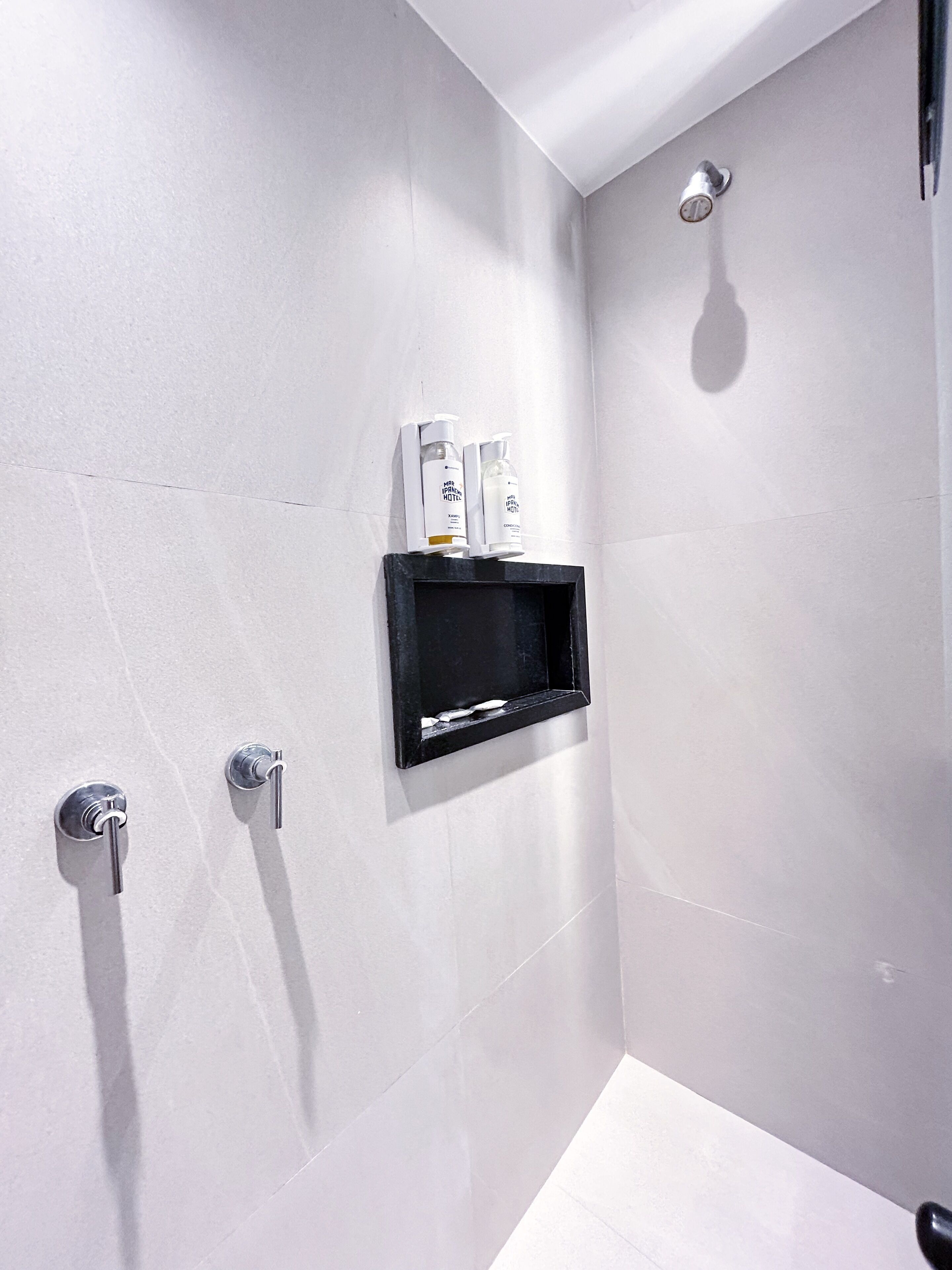 A modern bathroom with a shower, a black shelf with toiletries, and a wall-mounted faucet.