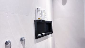 A modern bathroom with a shower, a black shelf with toiletries, and a wall-mounted faucet.