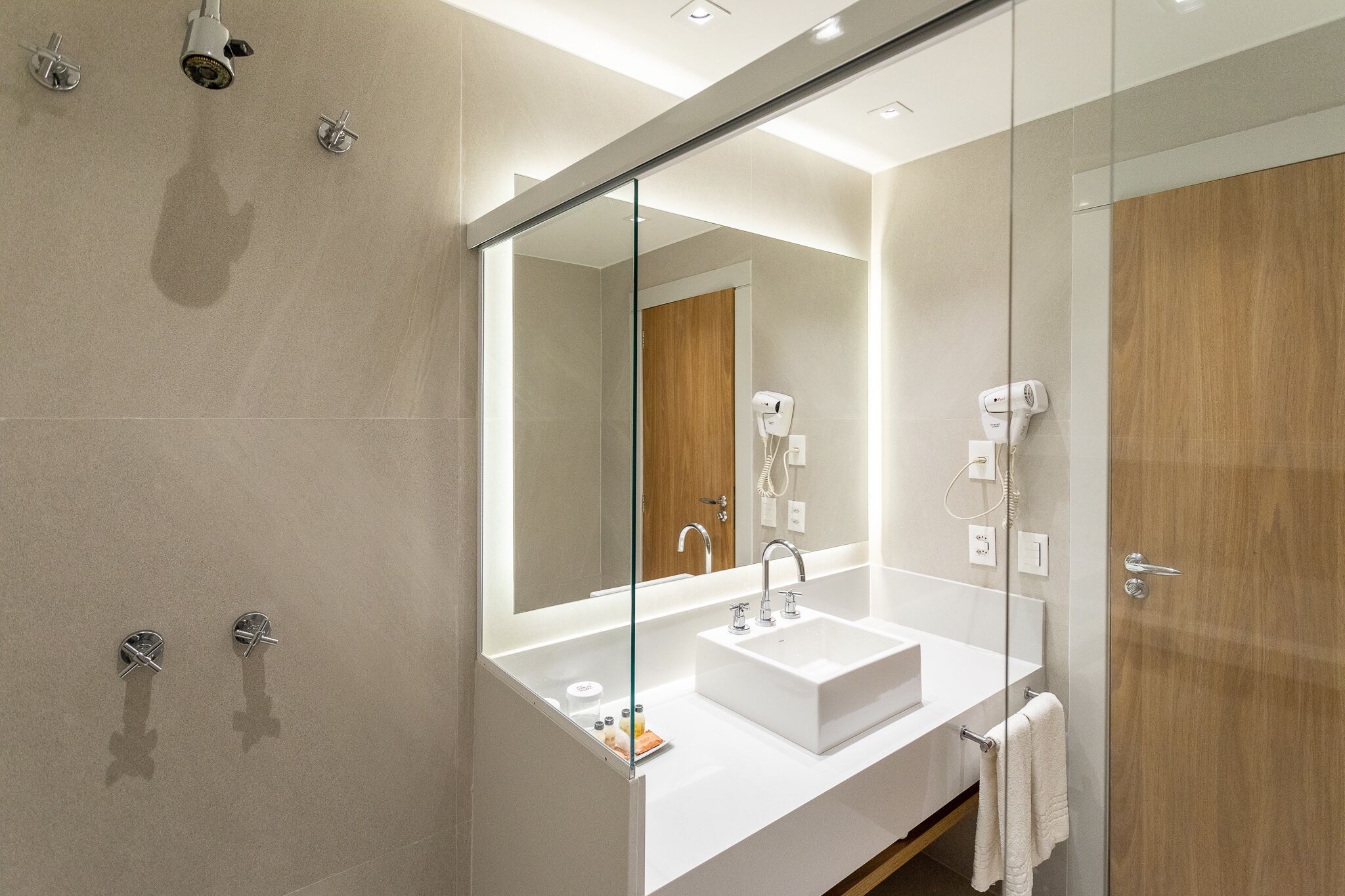 Un baño moderno con mampara de vidrio, un lavabo blanco y una puerta de madera.