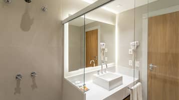 Un baño moderno con mampara de vidrio, un lavabo blanco y una puerta de madera.