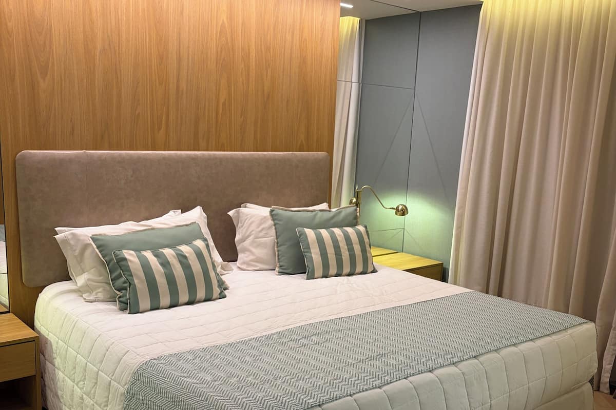 Una habitación de hotel moderna con una cama grande, paneles de madera, una mesita de noche y una mesita auxiliar.