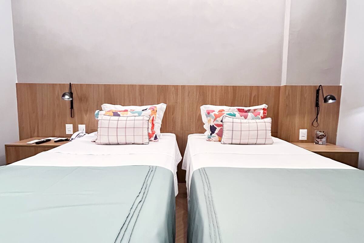 Habitación de hotel con dos camas, cada una con una almohada y una mesita de noche con lámpara.