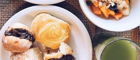 A breakfast setting with plates of scrambled eggs, toast, pastries, and a bowl of fruit salad.