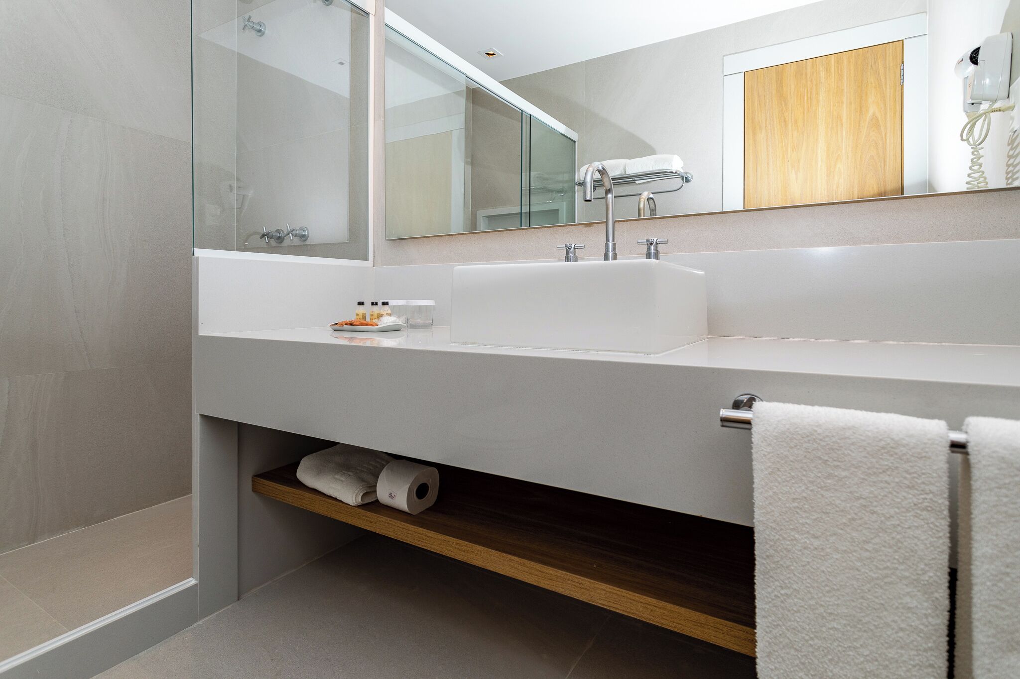 A modern bathroom with a large mirror, a white sink, and a towel rack.